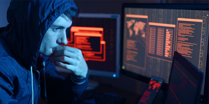 Hombre joven con gorra frente a monitores de computadora viendo código